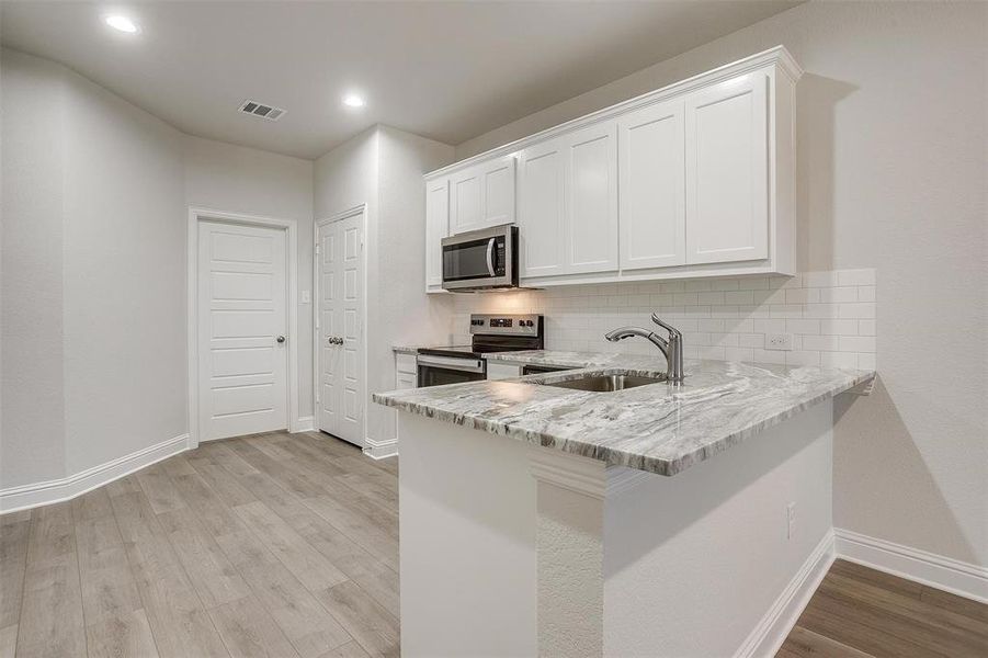 Kitchen with backsplash, appliances with stainless steel finishes, light wood-type flooring, white cabinets, and light stone counters