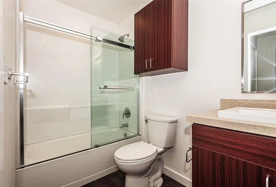 Full bathroom featuring shower / bath combination with glass door, hardwood / wood-style floors, vanity, and toilet