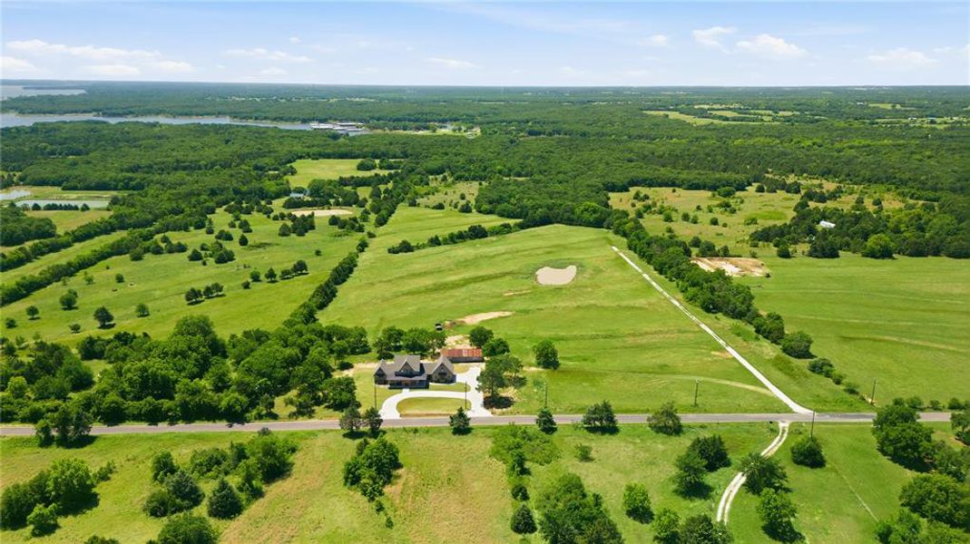 Expansive green landscape featuring a residence with an attached garage, a private driveway, and a pond