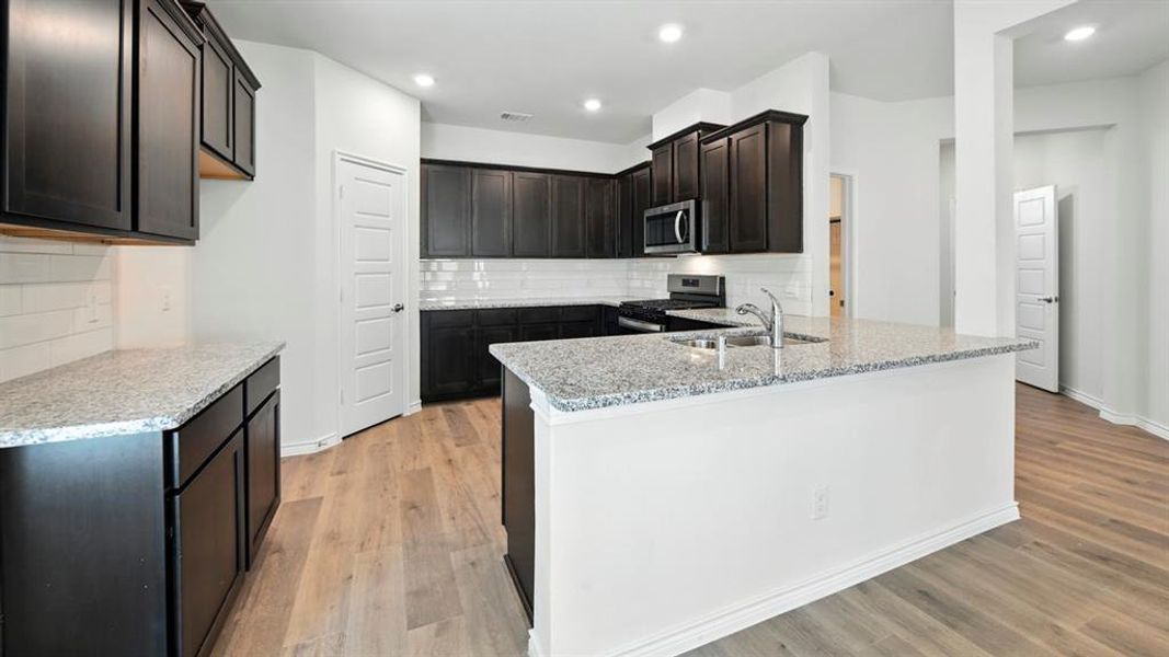 Kitchen with appliances with stainless steel finishes, light stone counters, a peninsula, light wood finished floors, and decorative backsplash