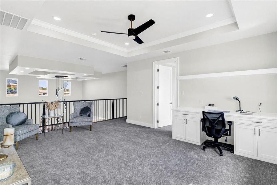 Carpeted office with crown molding, ceiling fan, built in desk, and a raised ceiling