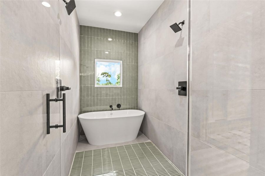 Inside view of the primary wet room/shower area featuring full wall tiling, a freestanding soaking tub nestled under a window, and a green-tiled accent floor. Inside view of the primary wet room/shower area featuring full wall tiling, a freestanding soaking tub nestled under a window, and a green-tiled accent floor.