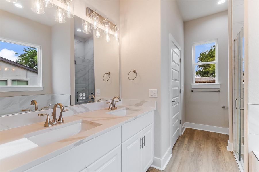 Bathroom featuring healthy amount of natural light, double vanity, wood finished floors, and a shower with door