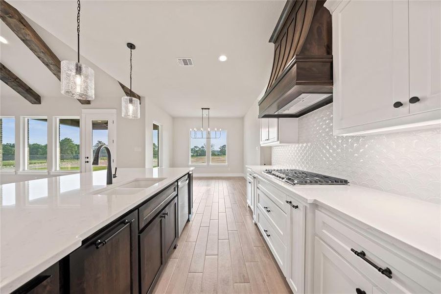 Kitchen featuring appliances with stainless steel finishes, custom range hood, light wood-type flooring, tasteful backsplash, and a sink Kitchen featuring appliances with stainless steel finishes, custom range hood, light wood-type flooring, tasteful backsplash, and a sink
