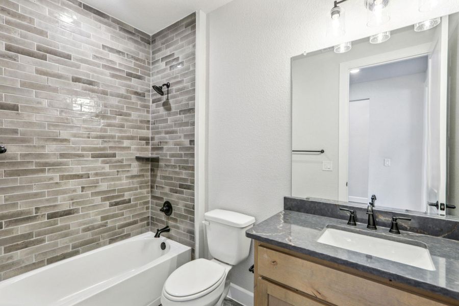 Full bath featuring washtub / shower combination, vanity, and a textured wall