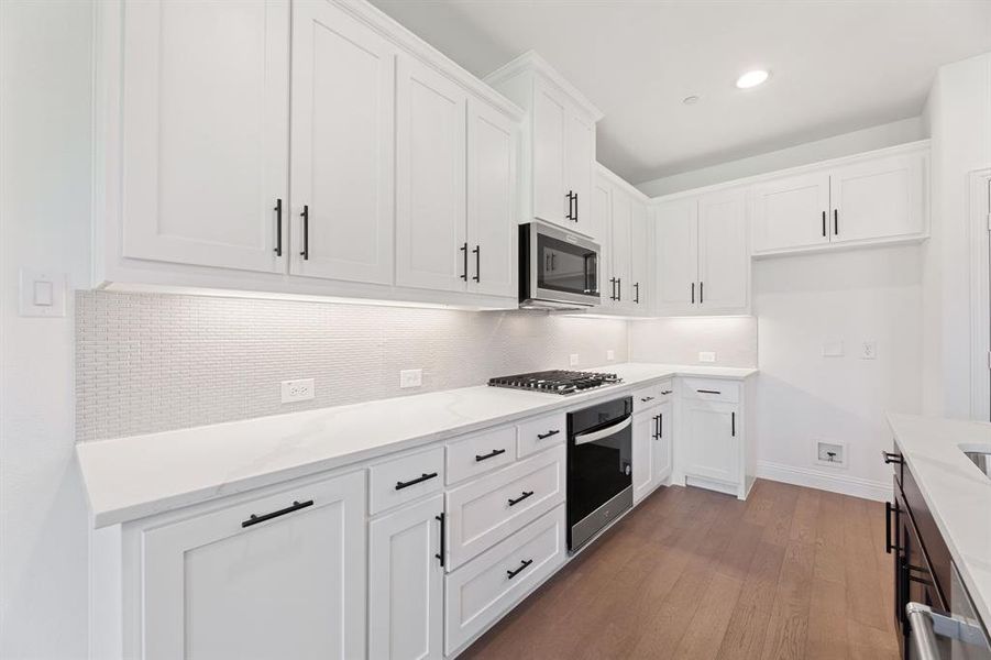 Kitchen featuring white cabinetry, tasteful backsplash, appliances with stainless steel finishes, dark wood finished floors, and light stone countertops Kitchen featuring white cabinetry, tasteful backsplash, appliances with stainless steel finishes, dark wood finished floors, and light stone countertops