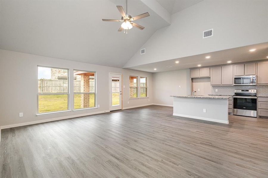 Kitchen with backsplash, high vaulted ceiling, gray cabinets, an island with sink, and appliances with stainless steel finishes