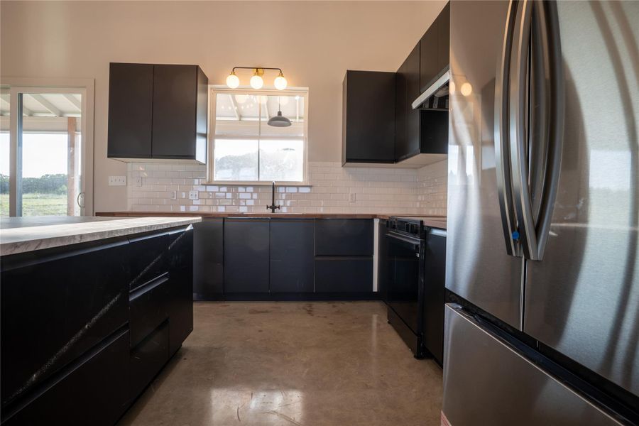 Kitchen featuring freestanding refrigerator, decorative backsplash, finished concrete flooring, and black electric range