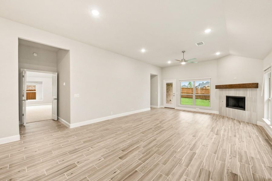 Open living room with wood-look tile floors, ceiling fan, fireplace, and sliding glass door to backyard Open living room with wood-look tile floors, ceiling fan, fireplace, and sliding glass door to backyard