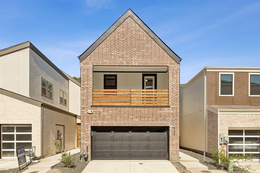 View of front facade with a garage, brick siding, driveway, and a balcony