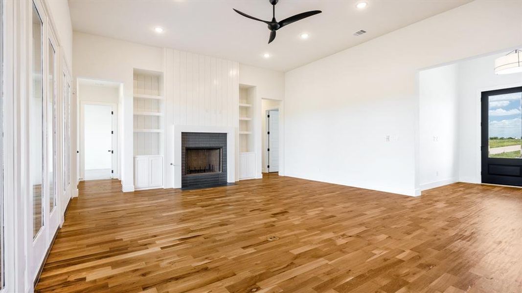 Unfurnished living room with a brick fireplace, ceiling fan, built in features, and light hardwood / wood-style flooring