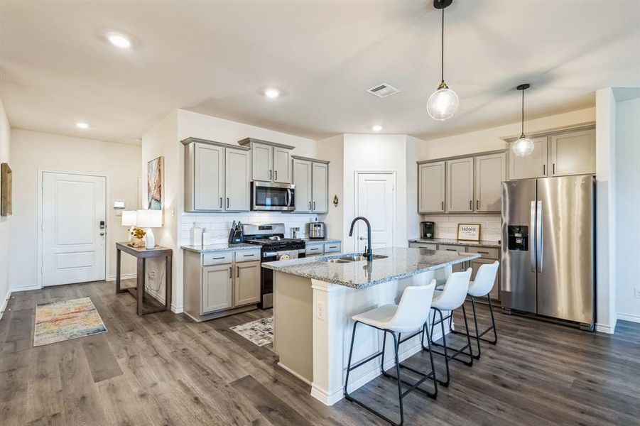 Kitchen featuring stainless steel appliances, sink, light stone counters, a center island with sink, and a breakfast bar area