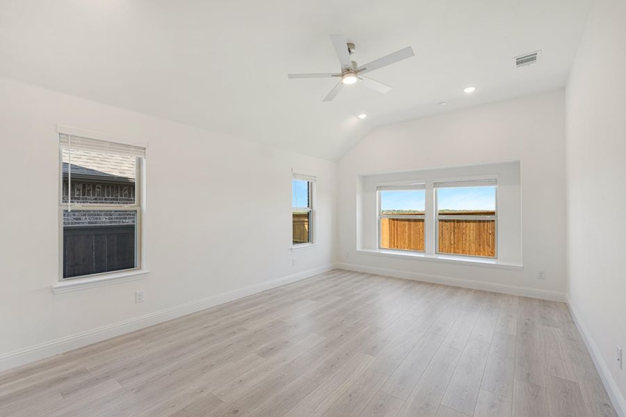 Empty room with vaulted ceiling, ceiling fan, light wood floors, and multiple windows Empty room with vaulted ceiling, ceiling fan, light wood floors, and multiple windows