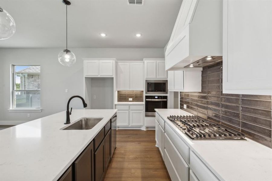 Kitchen with white cabinets, sink, appliances with stainless steel finishes, custom range hood, and light stone countertops