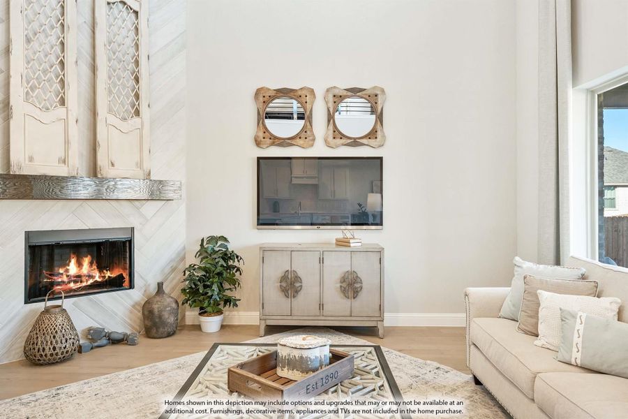 Living room with tall ceilings, lit fireplace, neutral sofa, and wall-mounted TV on light hardwood floors