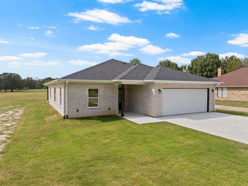 Ranch-style home with a front yard, driveway, brick siding, and roof with shingles