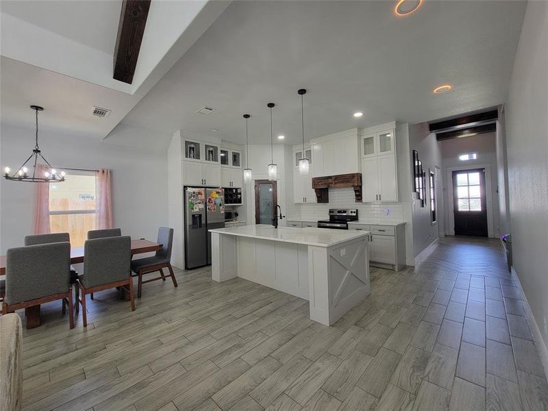 Kitchen featuring glass fronted cabinets, stainless steel appliances, white cabinetry, a kitchen island with sink, and backsplash