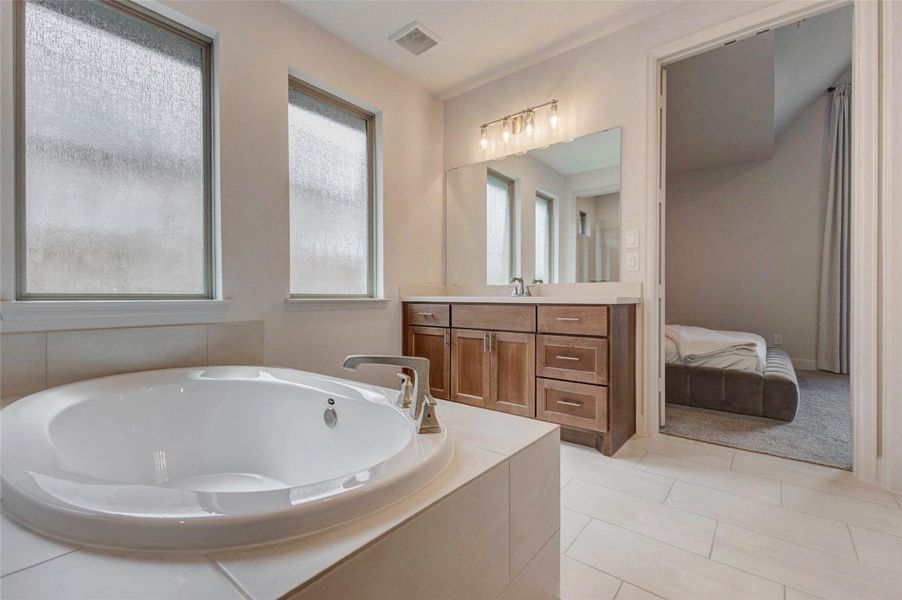 Llarge, white soaking tub, a double vanity with wooden cabinets, and frosted windows for privacy. The adjoining room has a cozy, carpeted area. Llarge, white soaking tub, a double vanity with wooden cabinets, and frosted windows for privacy. The adjoining room has a cozy, carpeted area.