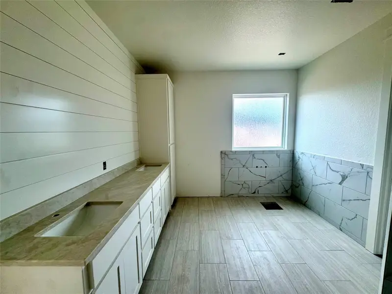 A spacious bathroom features dual vanities and tiled flooring, with an unfinished shower area awaiting completion.