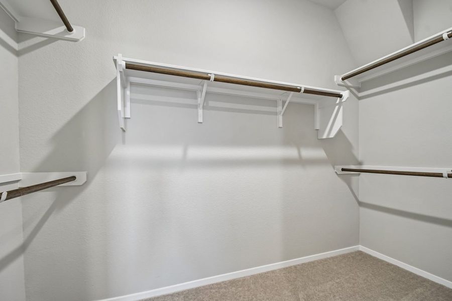 Image of walk-in closet with light carpet flooring and white walls. Two sets of closet rods on the left and right and a closet rod with shelf top in between