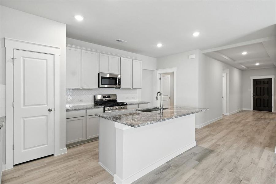 Kitchen featuring appliances with stainless steel finishes, an island with sink, light wood-style flooring, light stone countertops, and tasteful backsplash