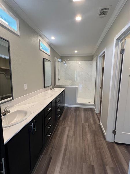Bathroom with a marble finish shower, double vanity, dark wood-style floors, crown molding, and a walk in closet