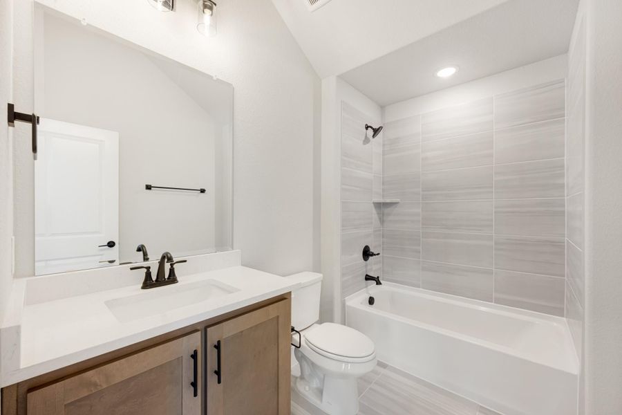 Bathroom with wood vanity, white quartz countertop, and tiled shower-tub combo with dark hardware Bathroom with wood vanity, white quartz countertop, and tiled shower-tub combo with dark hardware
