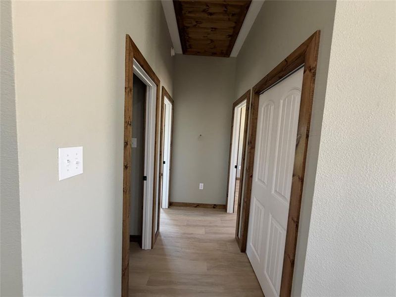Hallway featuring wood-finish flooring and multiple doorways with natural wood trim