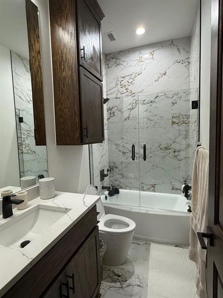 Full bathroom featuring light marble finish floors, vanity, and enclosed tub / shower combo