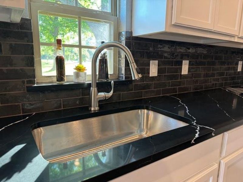 Room details featuring sink, white cabinets, and backsplash