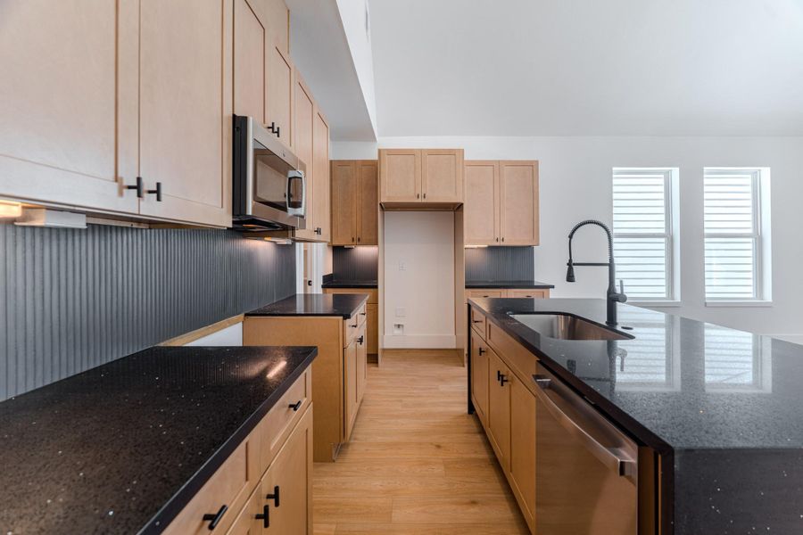 This modern kitchen features sleek black countertops, light wood cabinetry, and stainless steel appliances. It offers a spacious layout with a large island and a stylish, high-arc faucet. Natural light streams in through two large windows, creating a bright and inviting space.Photo Disclaimer: Photos are representative of the community and may depict a similar floor plan, model home, or previously completed residence. This modern kitchen features sleek black countertops, light wood cabinetry, and stainless steel appliances. It offers a spacious layout with a large island and a stylish, high-arc faucet. Natural light streams in through two large windows, creating a bright and inviting space.Photo Disclaimer: Photos are representative of the community and may depict a similar floor plan, model home, or previously completed residence.