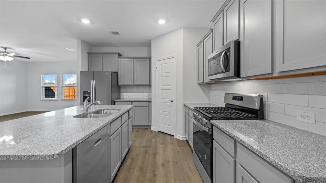 Kitchen with stainless steel appliances, dark wood-style floors, gray cabinetry, light stone counters, and a kitchen island with sink Kitchen with stainless steel appliances, dark wood-style floors, gray cabinetry, light stone counters, and a kitchen island with sink