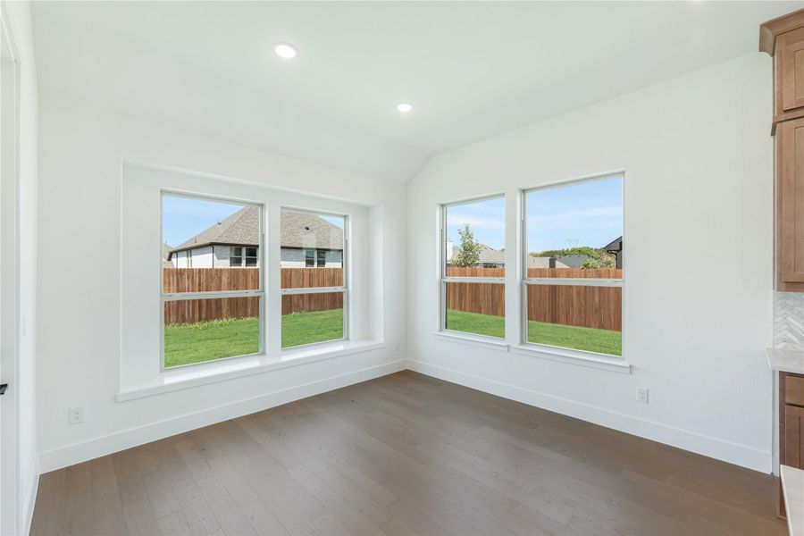 Empty room with hardwood floors, vaulted ceiling, and three windows overlooking a fenced backyard