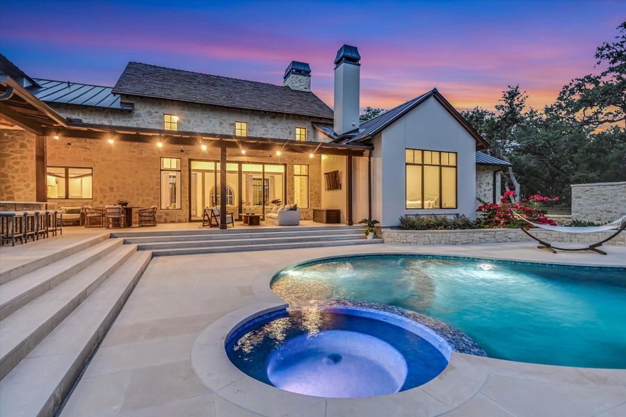 Back of property at dusk with a standing seam roof, a metal roof, a pool with connected hot tub, and a patio area Back of property at dusk with a standing seam roof, a metal roof, a pool with connected hot tub, and a patio area