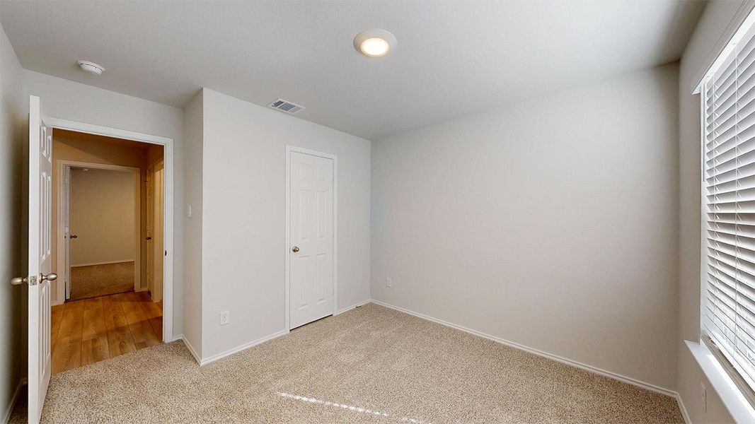 A well-lit bedroom with soft carpet offers a comfortable retreat, enhanced by natural light from a window with blinds.