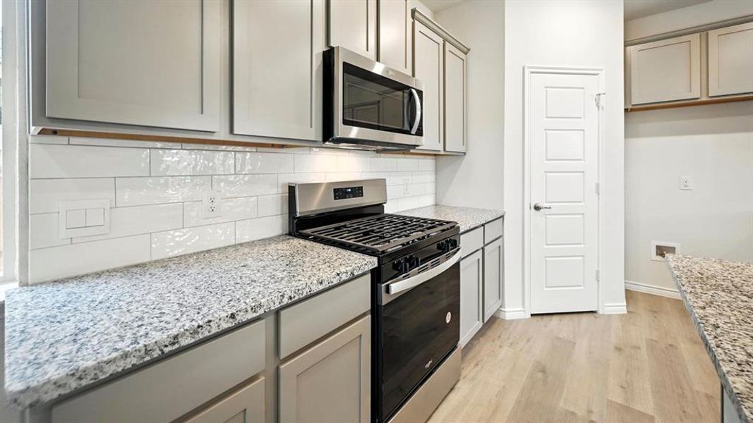 Kitchen with stainless steel appliances, light wood finished floors, light stone counters, and tasteful backsplash Kitchen with stainless steel appliances, light wood finished floors, light stone counters, and tasteful backsplash