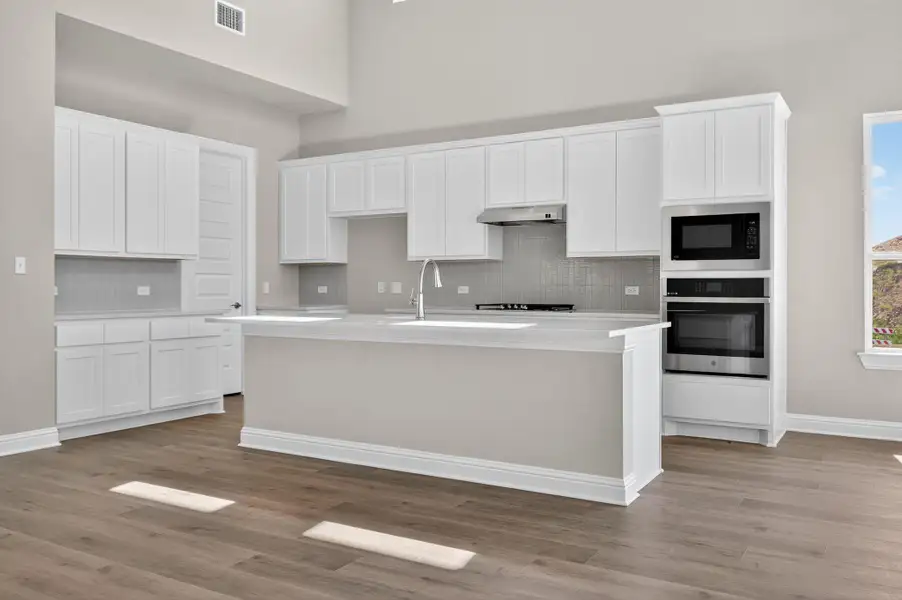 Kitchen with stainless steel oven, white cabinetry, tasteful backsplash, a center island with sink, and a high ceiling