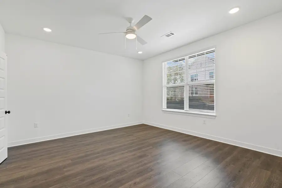 Spacious room featuring wood-finish flooring, white walls, and a ceiling fan with integrated lighting
