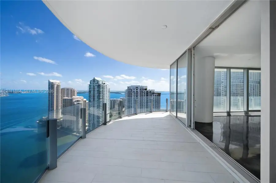 Wraparound balcony featuring large-format tile flooring, a glass panel railing, and expansive floor-to-ceiling glass sliding doors Wraparound balcony featuring large-format tile flooring, a glass panel railing, and expansive floor-to-ceiling glass sliding doors