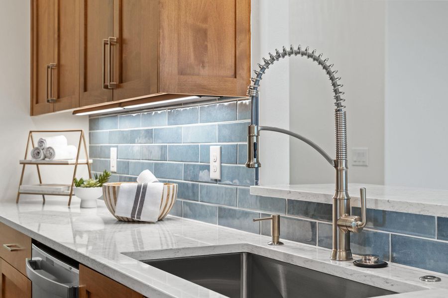 Kitchen view of custom cabinetry, decorative backsplash, a sink, and light stone counters Kitchen view of custom cabinetry, decorative backsplash, a sink, and light stone counters