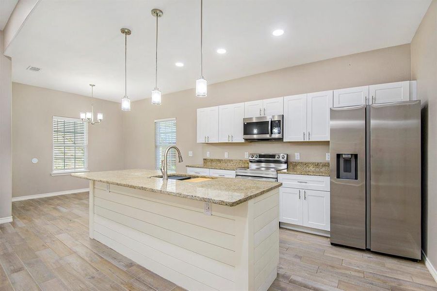 Kitchen featuring stainless steel appliances, light wood-type flooring, a chandelier, white cabinetry, and a kitchen island with sink