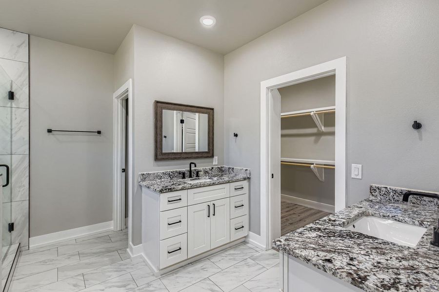Full bathroom featuring two vanities, light marble finish flooring, a stall shower, and a walk in closet