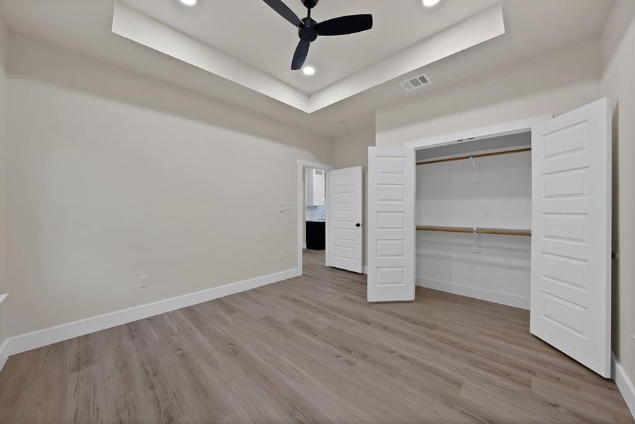Unfurnished bedroom with a tray ceiling, light wood-type flooring, ceiling fan, a closet, and recessed lighting