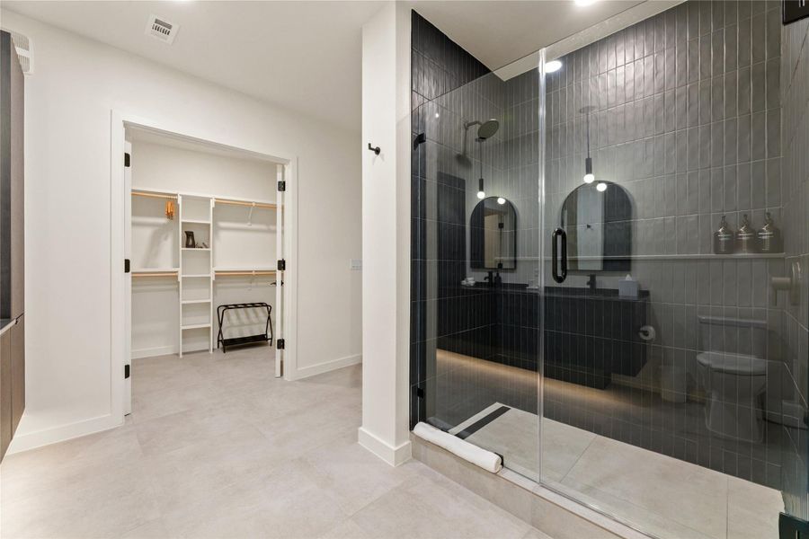 A sleek walk-in shower features vertical tiling, leading seamlessly to an adjacent closet space. A sleek walk-in shower features vertical tiling, leading seamlessly to an adjacent closet space.
