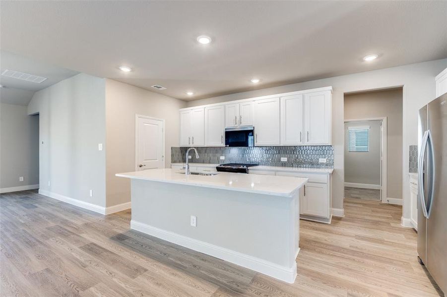 Kitchen with backsplash, white cabinets, a center island with sink, stainless steel appliances, and light stone countertops Kitchen with backsplash, white cabinets, a center island with sink, stainless steel appliances, and light stone countertops
