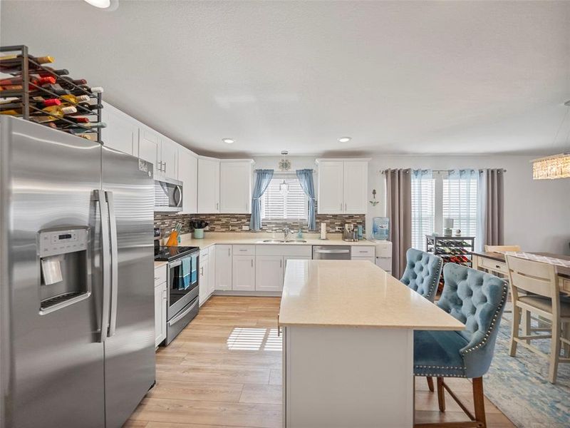 Kitchen featuring white cabinetry, light countertops, appliances with stainless steel finishes, backsplash, and a center island