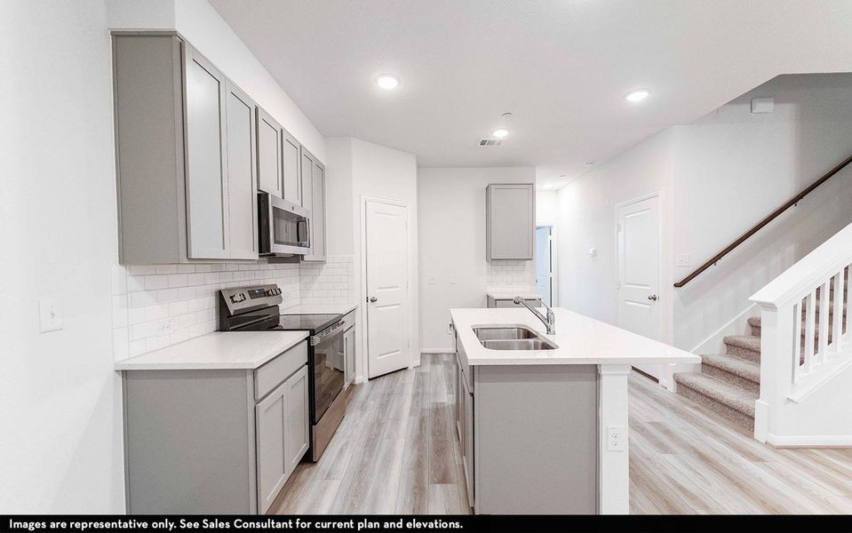 Kitchen with gray cabinetry, stainless steel appliances, a center island with sink, tasteful backsplash, and light wood-style floors