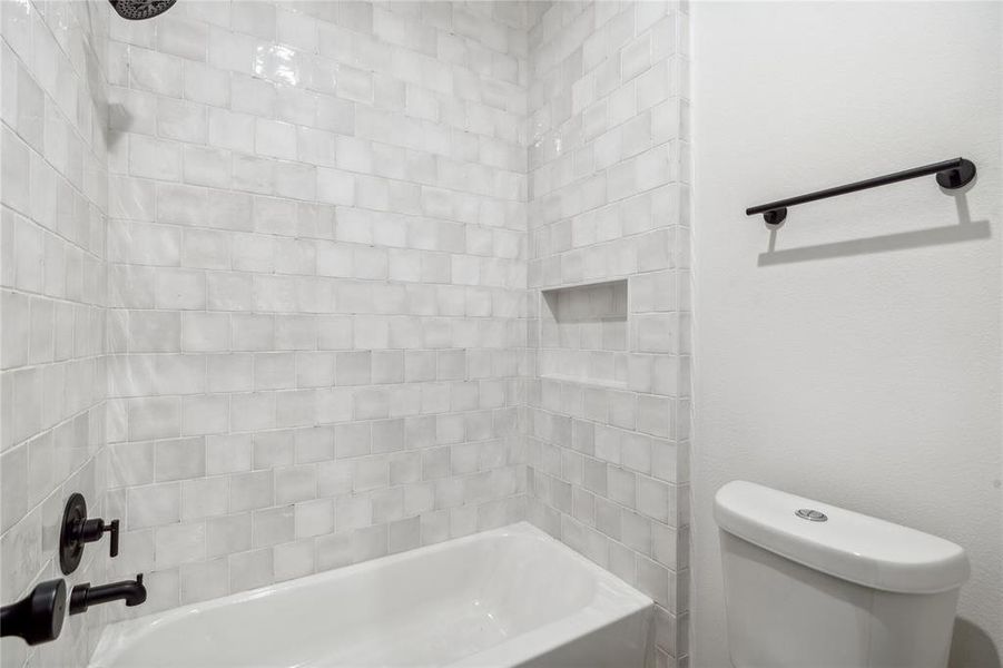 This secondary bathroom features a beautifully tiled bathtub with floor-to-ceiling subway tiles, creating a sleek and modern look that makes the space feel both spacious and elegant.