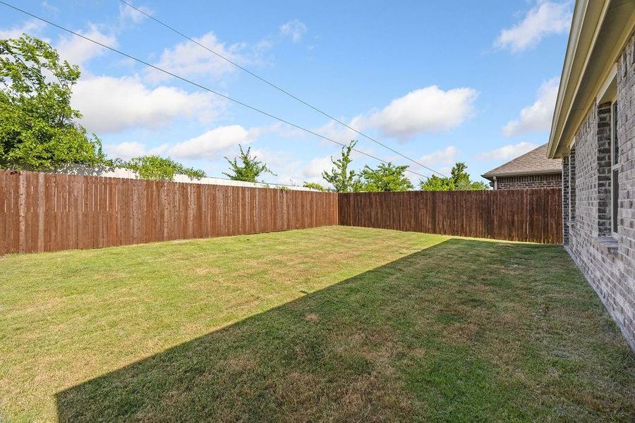 Expansive backyard featuring a manicured lawn, full privacy fencing, and a brick exterior facade Expansive backyard featuring a manicured lawn, full privacy fencing, and a brick exterior facade
