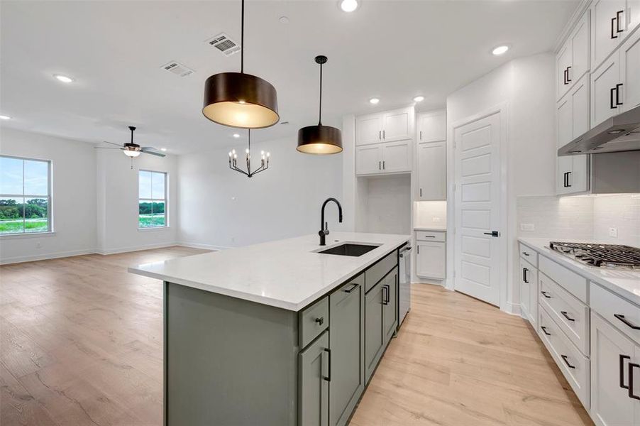Open-concept kitchen featuring an island with a built-in sink, white countertops, a gas range with an overhead vent, and wood-finish flooring throughout Open-concept kitchen featuring an island with a built-in sink, white countertops, a gas range with an overhead vent, and wood-finish flooring throughout